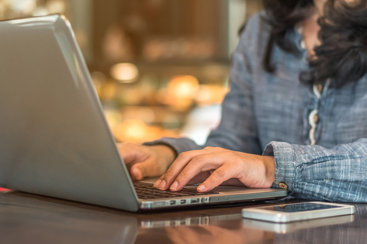 Person typing on a laptop at a table with a smartphone nearby in a casual workspace.