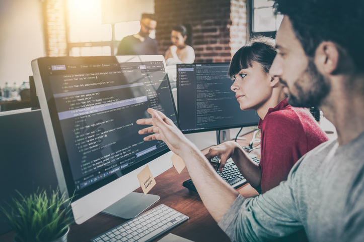 Two software developers reviewing code on a desktop computer during a collaborative work session in an office.