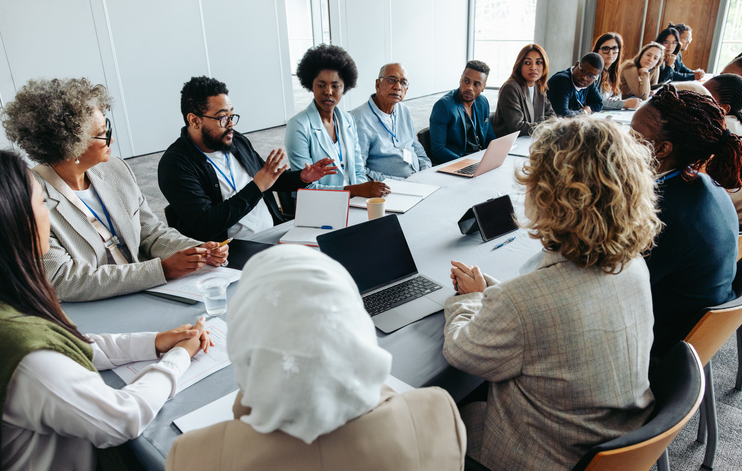 Diverse group of professionals seated around a conference table, participating in a team discussion during a meeting.