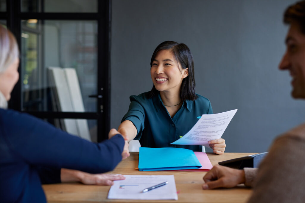 smiling asian woman shaking hands with a candidate during an interview.